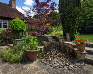 stone water feature in garden with potted trees