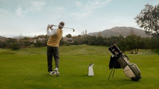 A golfer hits a shot on the driving range next to the Garmin Approach R50 launch monitor