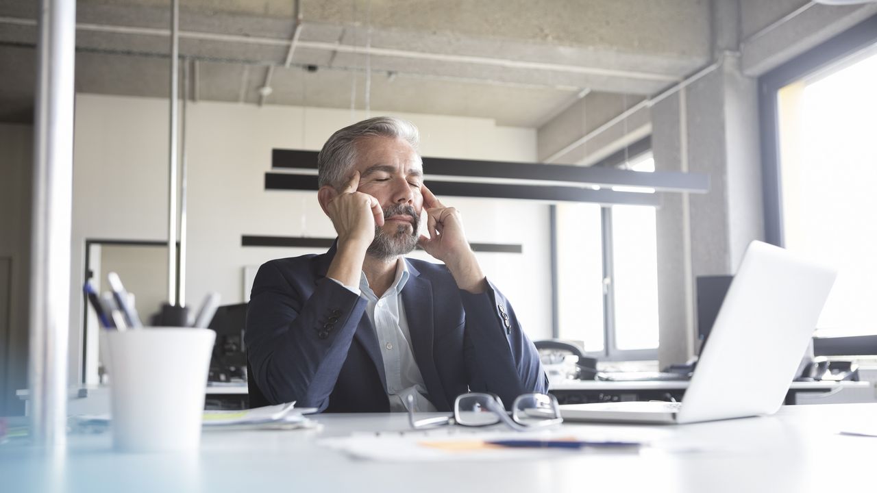 Businessman sitting at his desk rubs his temples like he has a headache.