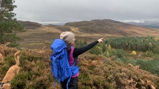 Hiker pointing across the landscape while wearing a blue backpack