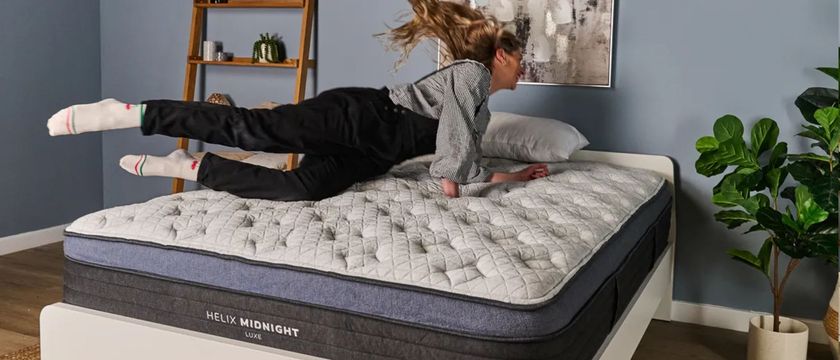 The image shows a light haired woman smiling as she dives onto a mattress that is placed in a pale blue bedromm