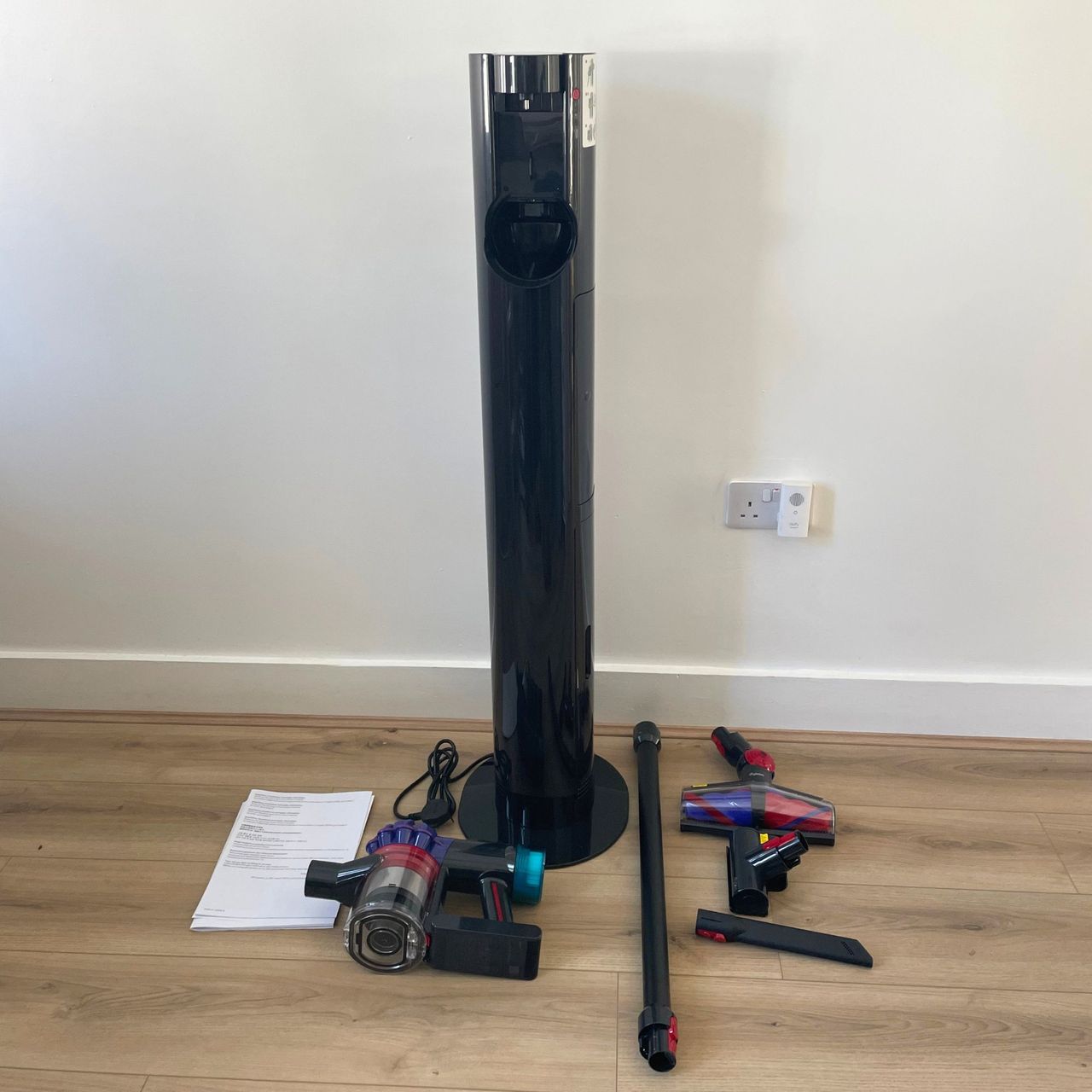 Dyson V10 Konical Cordless Vacuum and Auto-Empty Dok and its components laid out on wood-effect flooring in front of a white wall