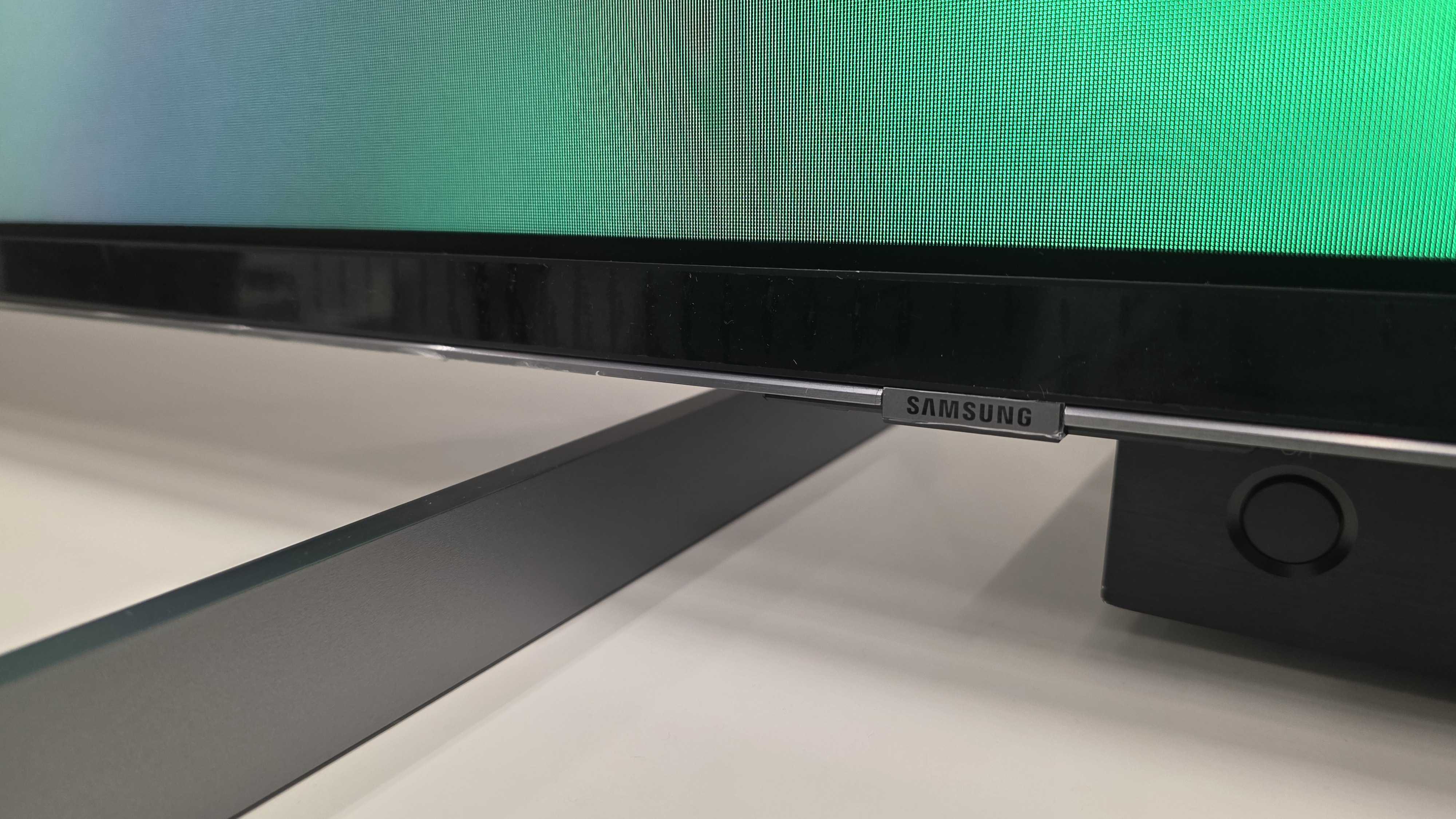 A 115-inch Samsung RGB LED TV on a white stand with colourful demo content on screen featuring the Statue of Liberty and a hot air balloon made of roses.