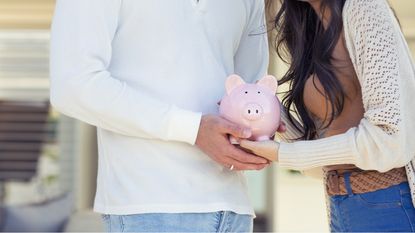 A couple hold a piggy bank between them.