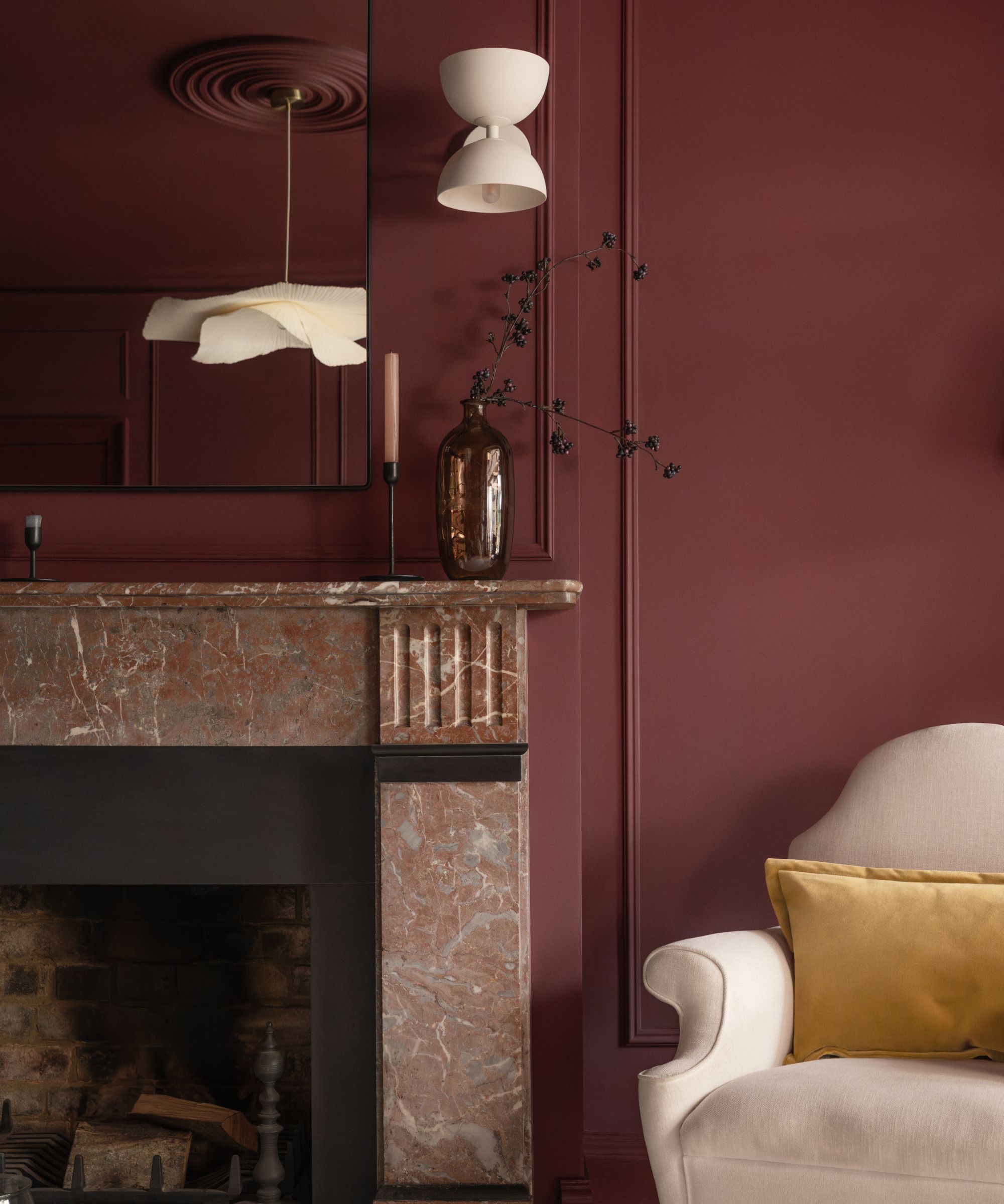 A living room with dark red walls and a marble fireplace, and a beige armchair in the corner.