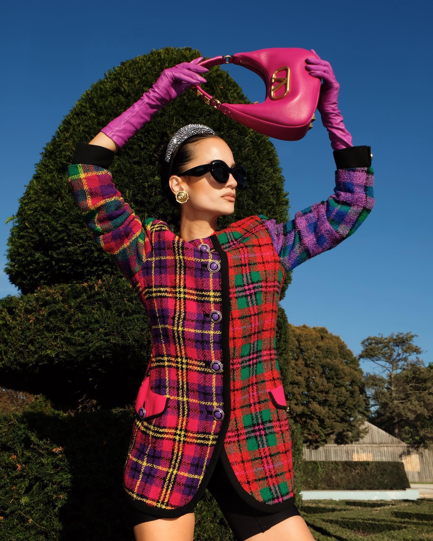 Anna posing wearing a tartan check blazer dress, long gloves and holding a pink Valentino bag over her head