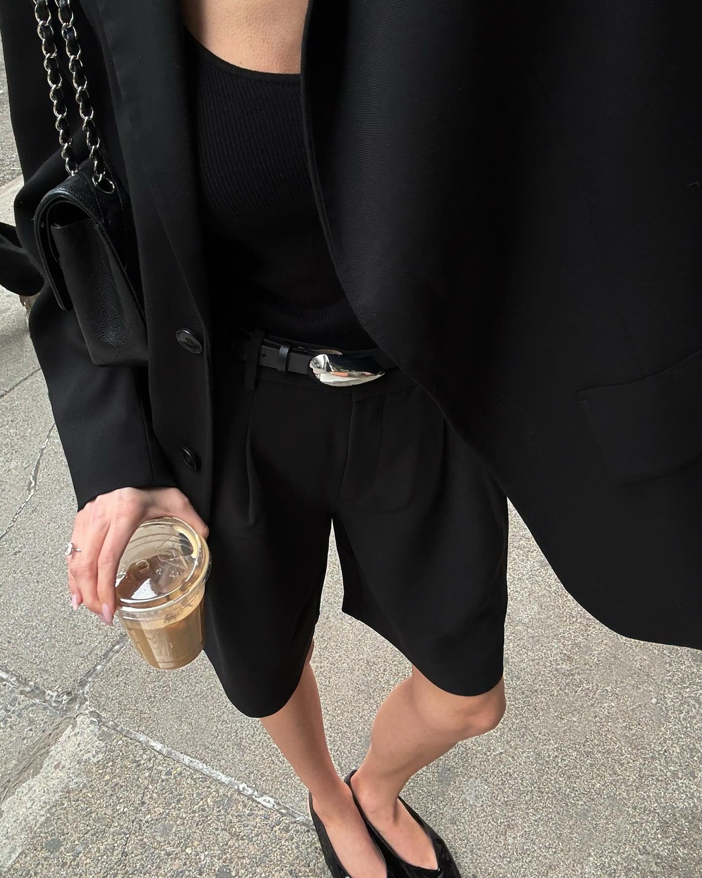 close up of style influencer Fredrika Galgano wearing an all-black outfit idea with a Chanel bag, black blazer, basic top, Heaven Mayhem statement belt, Bermuda shorts, and black flats