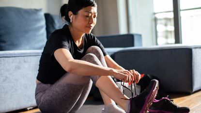 Woman sits on floor tying up running shoes