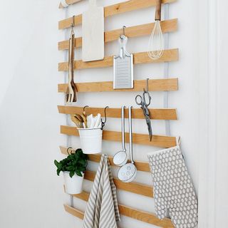 Small kitchen items hung from a wooden slatted hanger on kitchen wall