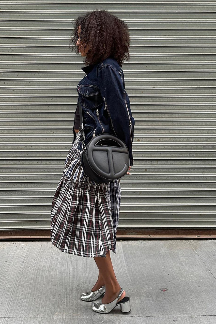 A woman wearing a denim jacket, plaid skirt, and silver shoes