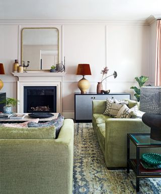 living room with green sofas, fireplace, warm gray paneled walls, gold mirror and patterned rug