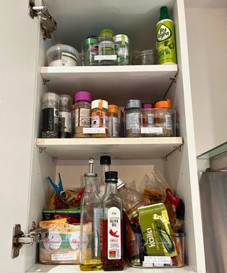 My open spice cabinet with three shelves and clear containers with herb jars. The bottom shelf has the tallest space and houses oil jars as well