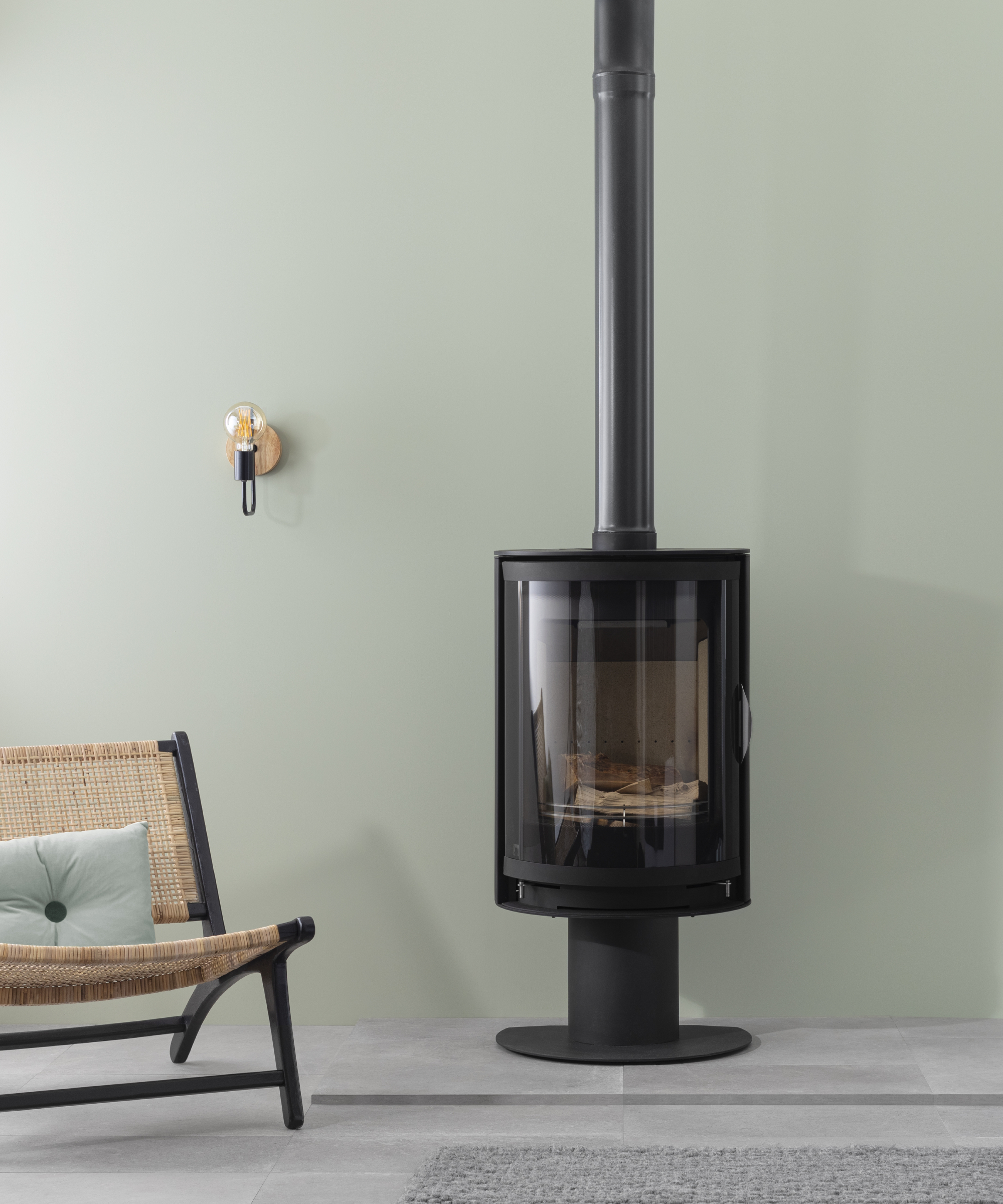 black floor mounted cylinder log burner with tall flue in room with pale green wall and light tiled floor