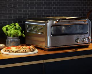 Pizzaiolo indoor pizza oven by Sage appliances with pizza laid on top of pizza stone on kitchen worktop