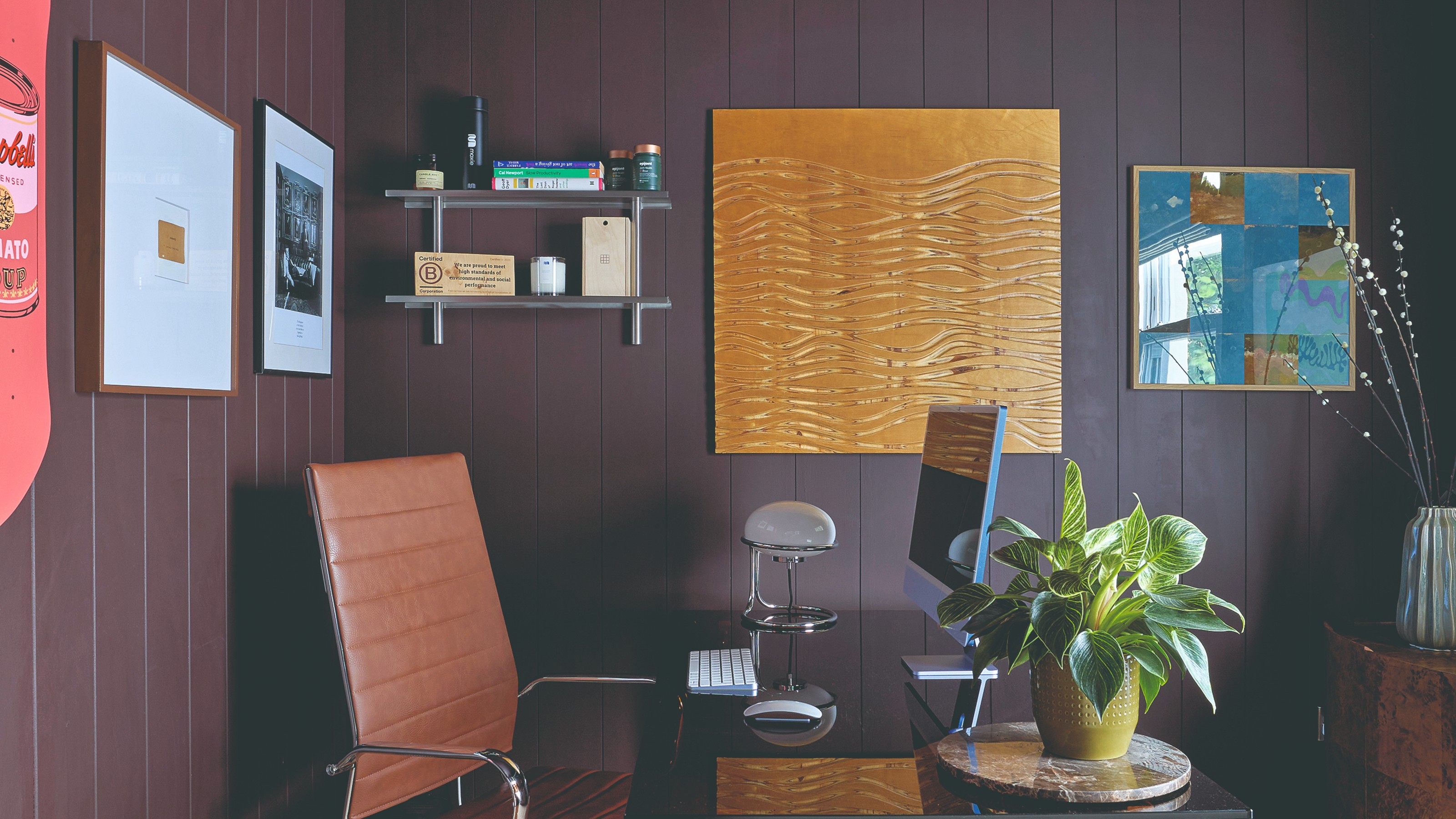 An aubergine purple-painted home office with wall panelling and art hung on the walls, with one of the frame being extra sizes compared to the artwork within