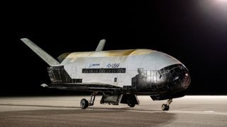 a black and white space plane sits on a runway at night.