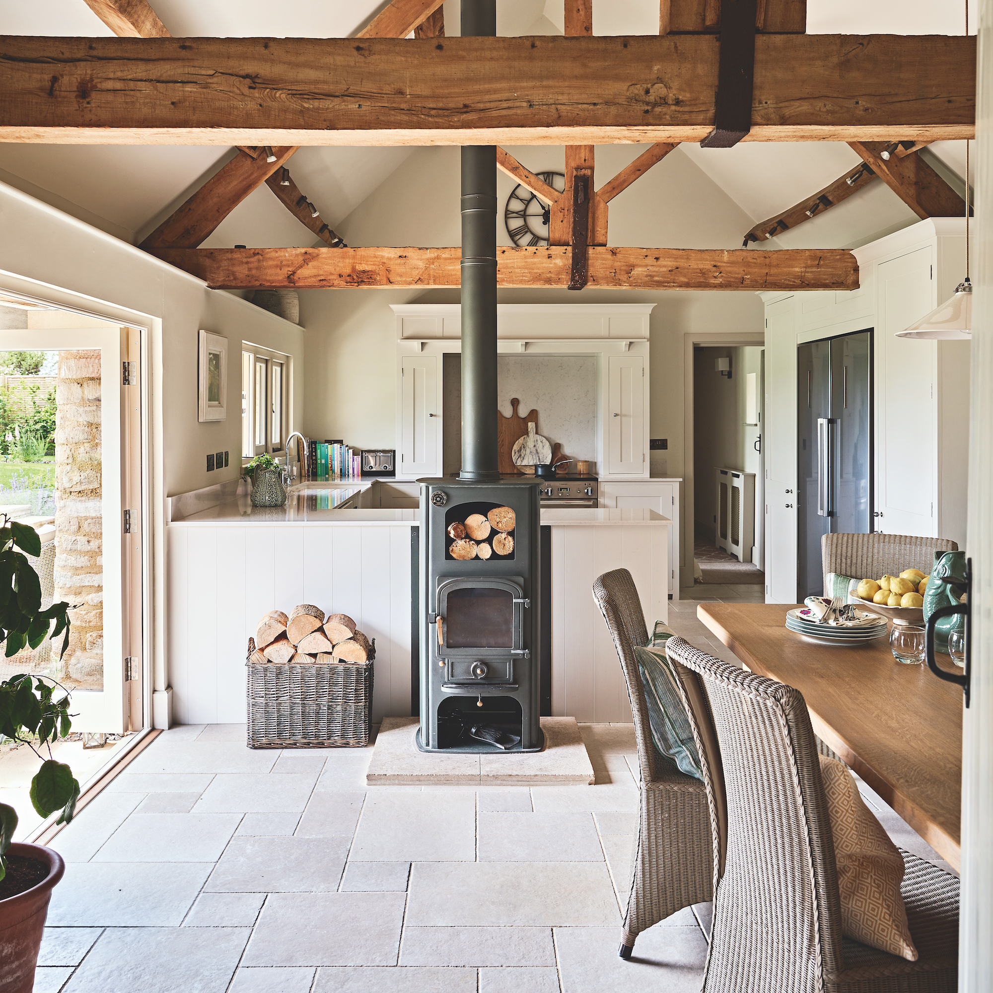 dining room in converted cowshed with woodburner stove and farmhouse table with wicker dining chairs