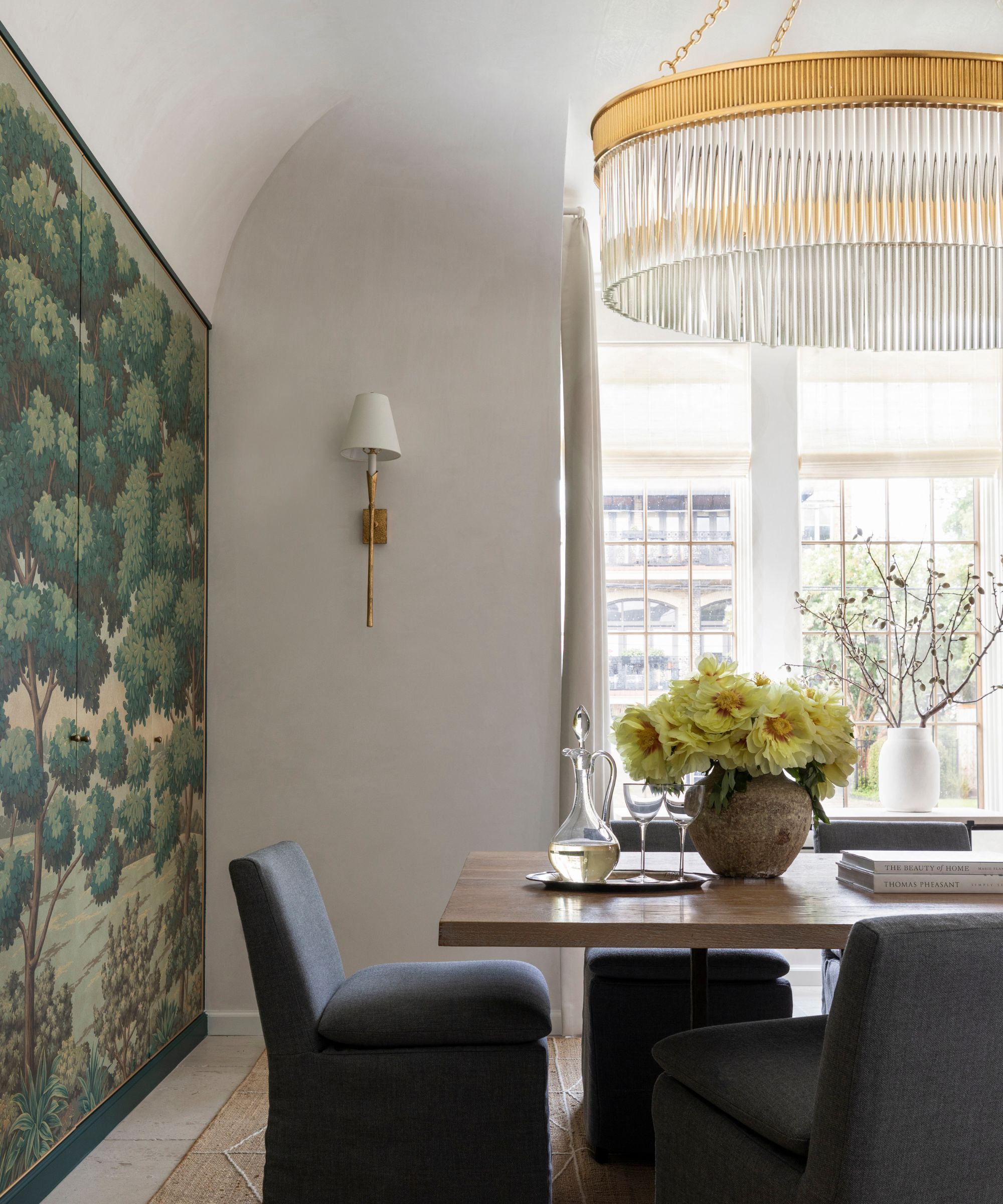 white painted dining room with a large gold and crystal chandelier with a wood table, navy slip covered dining chairs with a large wall tapestry
