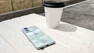 The OnePlus Nord 2T, laid face down on a stone bench next to a paper coffee cup
