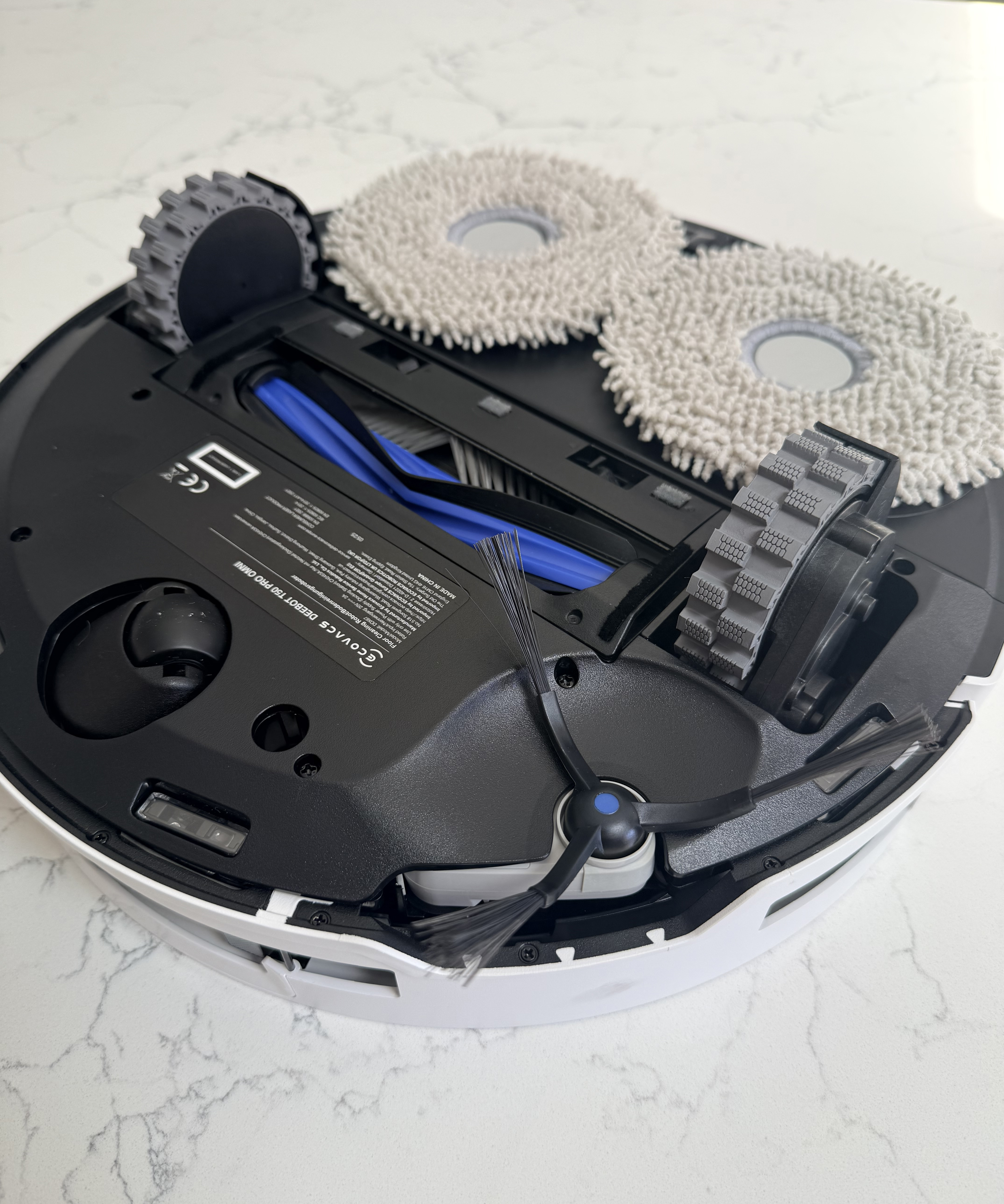 Underside of the Ecovacs Deebot T50 Pro Omni showing the rubber main brush, side brush, drive wheels and dual spinning mop pads