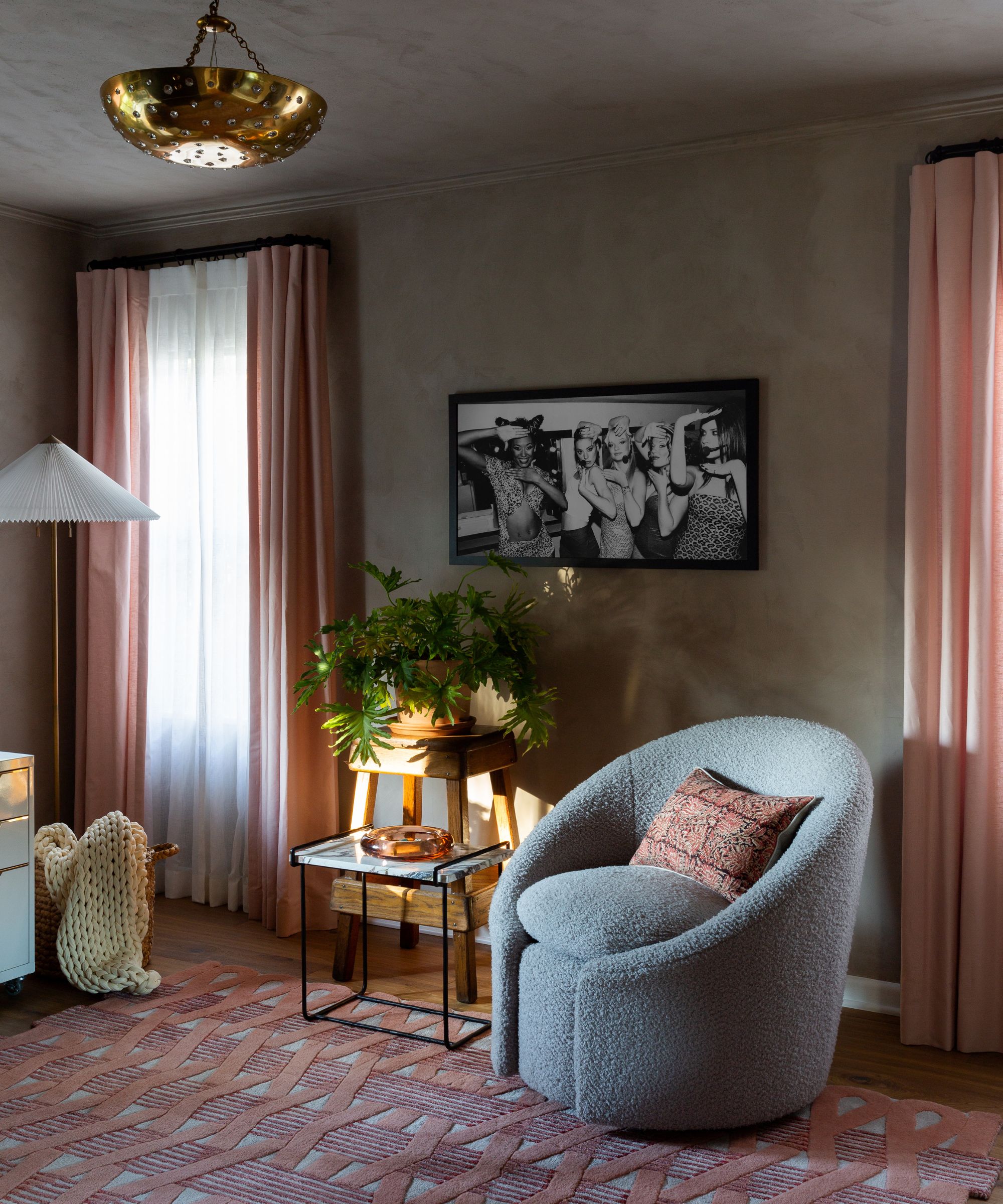 living room with taupe walls, pink rug and curtains, and gray boucle armchair with pink cushion