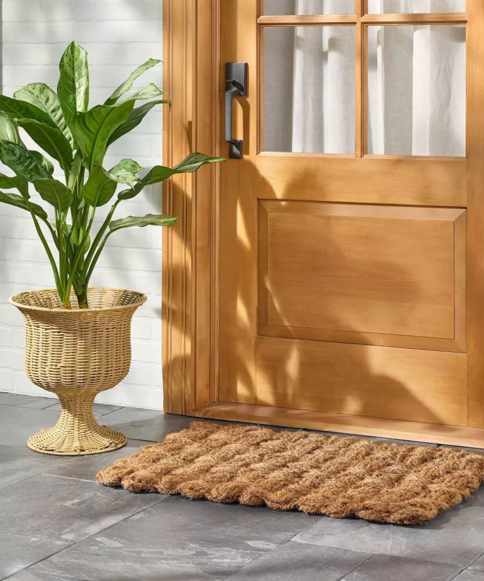 a front door with a doormat and a woven rattan planter with a tall plant inside