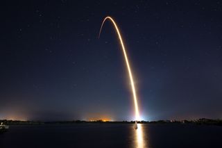 a rocket streaks across the night sky reflected in water