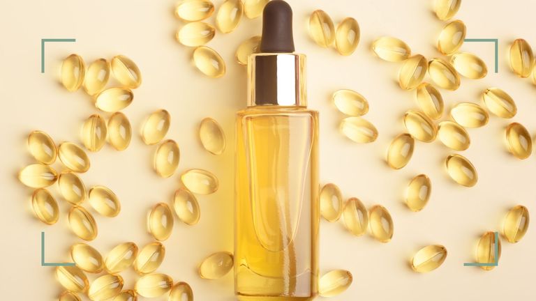A bottle of Vitamin E oil with capsules behind on a cream backdrop