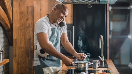 A man smiles as he talks on the phone while cooking