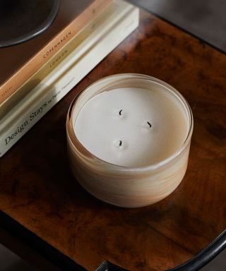 dark wood side table with a large beige candle and a stack of neutral coffee table books