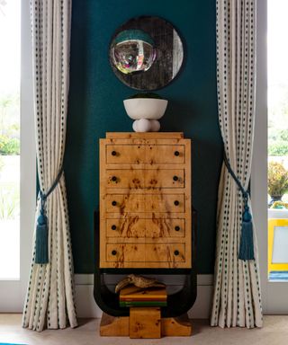 dark teal wall with wooden cabinet, cream and blue patterned drapes