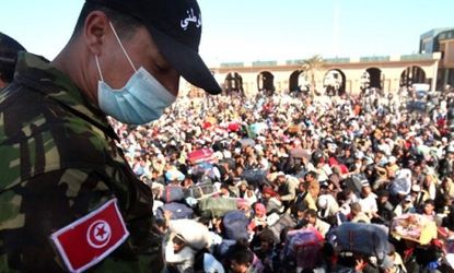 A guard watches over thousands of Libyan men waiting to enter Tunisia.