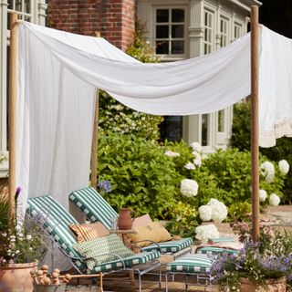 White curtain draped over timber structure with striped garden loungers