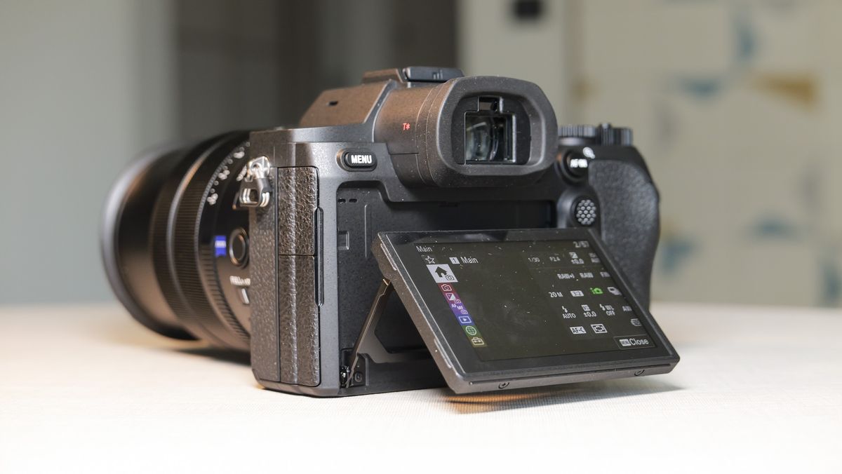 The Sony RX10 V bridge camera on a white table with a patterned wallpaper background, view of its rear, with the screen titled