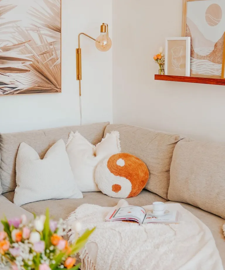 A gray couch with white throw pillows and a blanket with a magazine on it