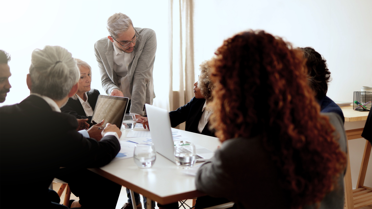 Several business people sitting round a table with one man standing