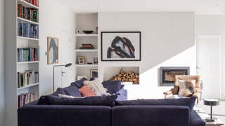 Living room with book shelf to the left, blue L shaped sofa and alcove shelving and log store
