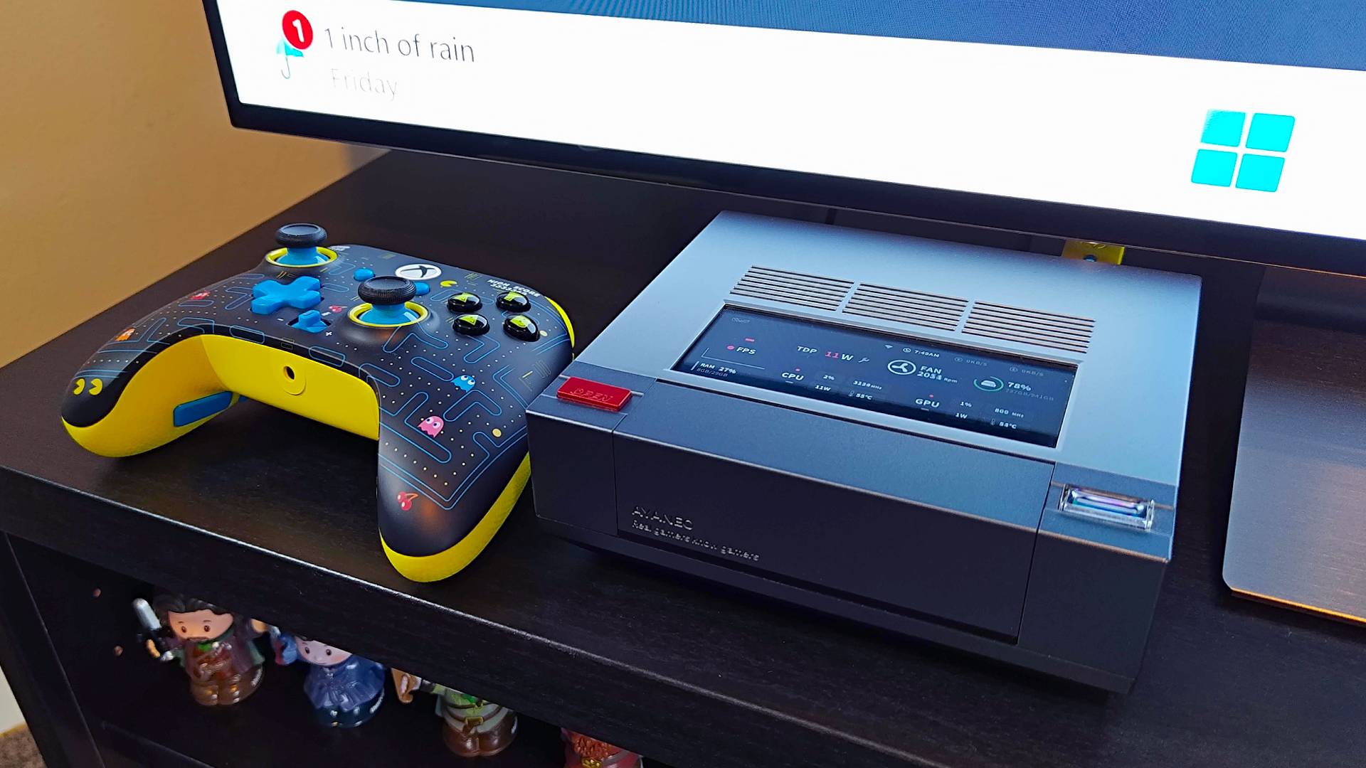 Ayaneo Mini PC AM02 sitting on TV bench next to Pac-Man controller.