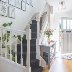 White hallway with wooden flooring and a blue stair runner. The white front door is partially open