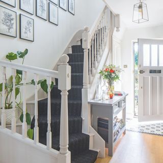 White hallway with wooden flooring and a blue stair runner. The white front door is partially open