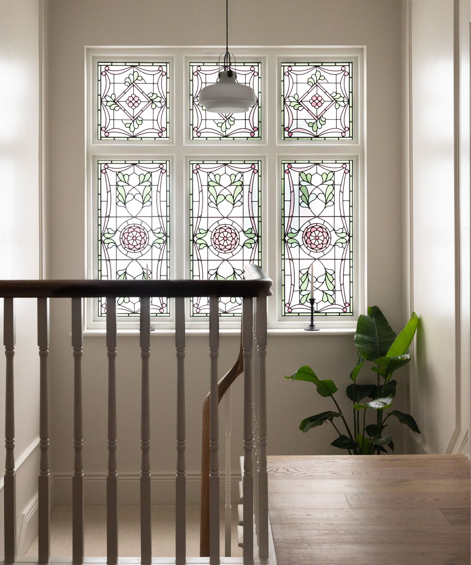 Bright stairwell with decorative stained glass windows, white walls and wooden accents, creating a light-filled, traditional-meets-modern space.