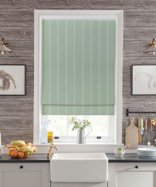 Sage green roman blind in kitchen above white sink with gray paneled walls and dark countertops