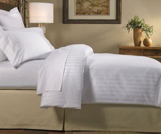 Side view of duvet and pillows on a Marriott bed against a beige wall.