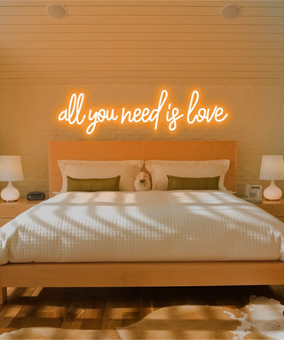 A warm neon sign reading "all you need is love" in a warm sunset bedroom