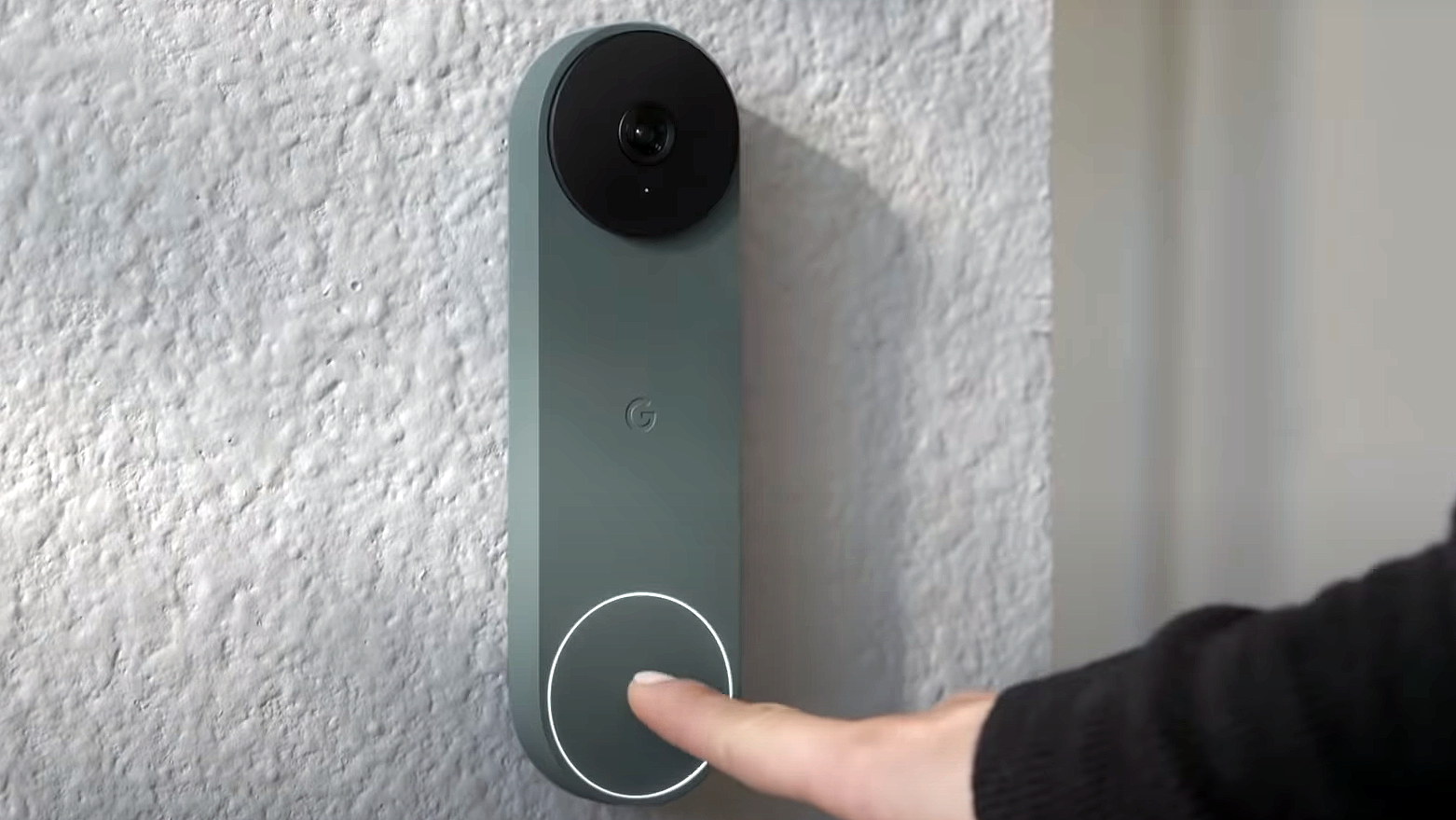A green Nest Doorbell against a white wall, being pressed
