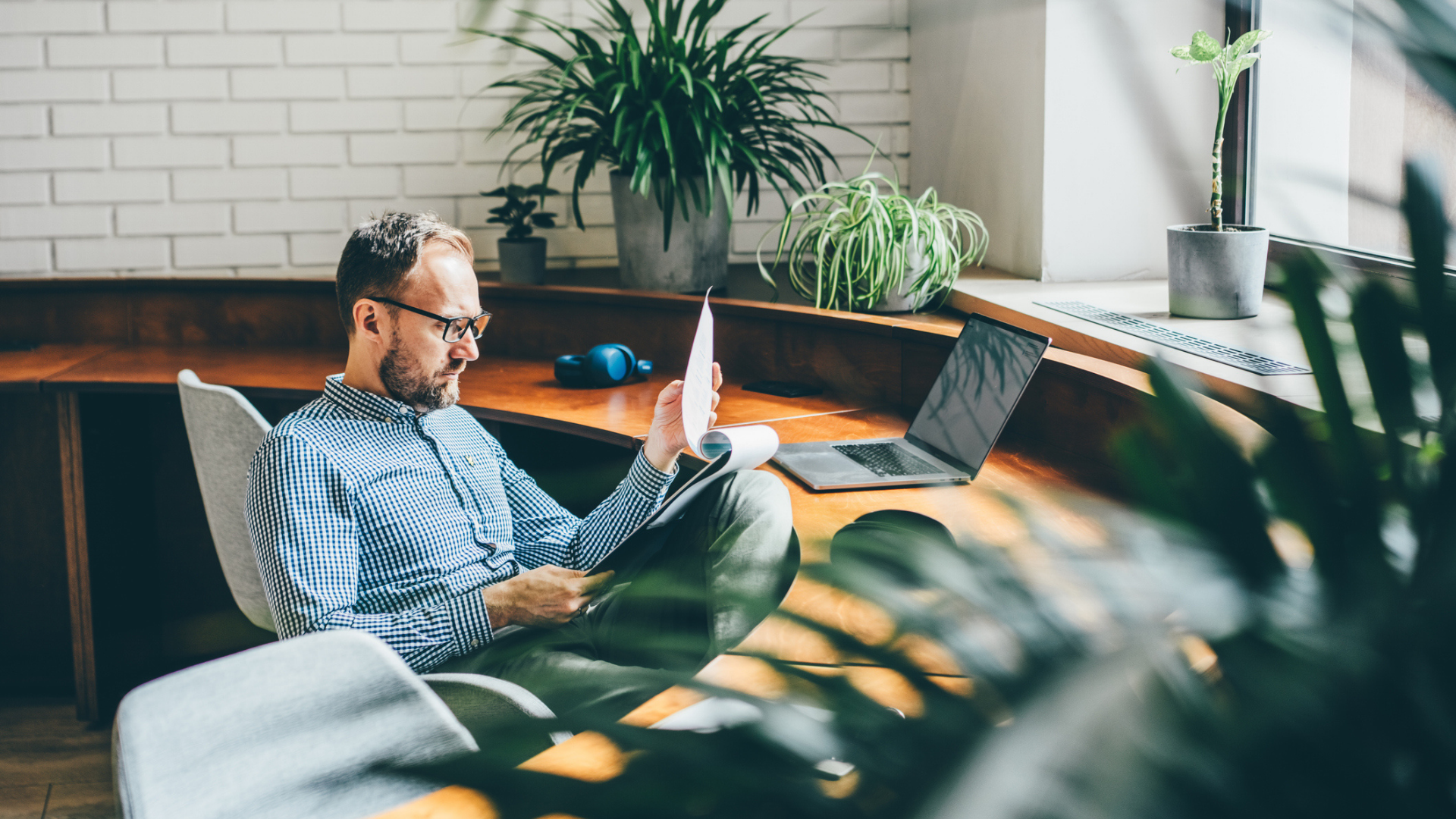 A man in a home office in front of a laptop on a desk while reading reports