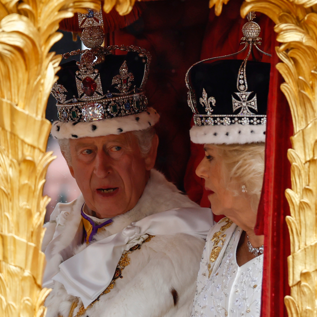 Queen Camilla and King Charles riding in a gold carriage wearing crowns
