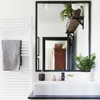 White bathroom with large black framed mirror and pot plants