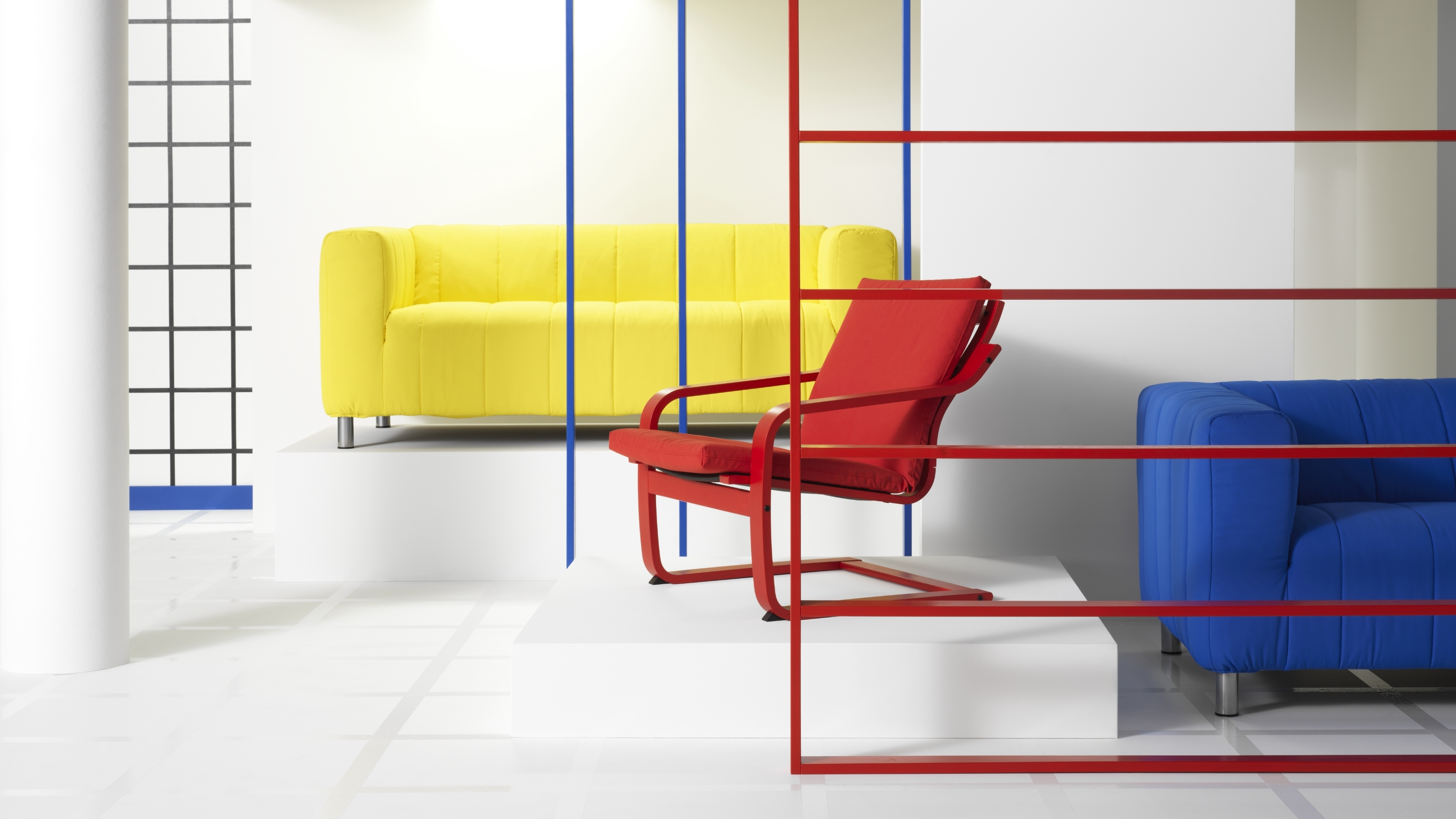 A white room with industrial frames in primary colors and a red POANG recliner chair