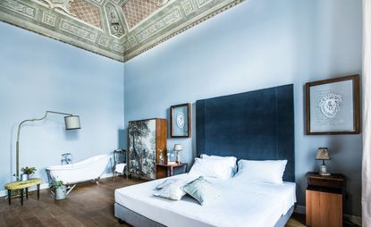 Guest room in pale blue with a navy velvet headboard, free-standing bath and dark wood floors